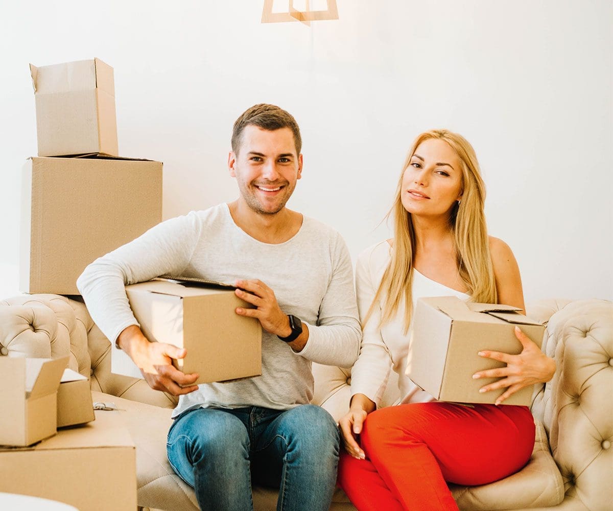 Man and woman sitting on couch holding moving boxes
