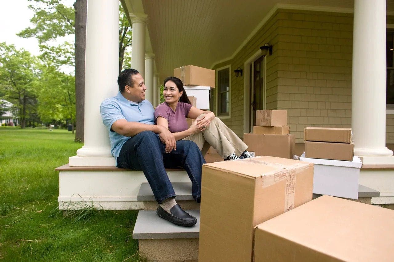 Couple sitting on front deck with moving boxes smiling